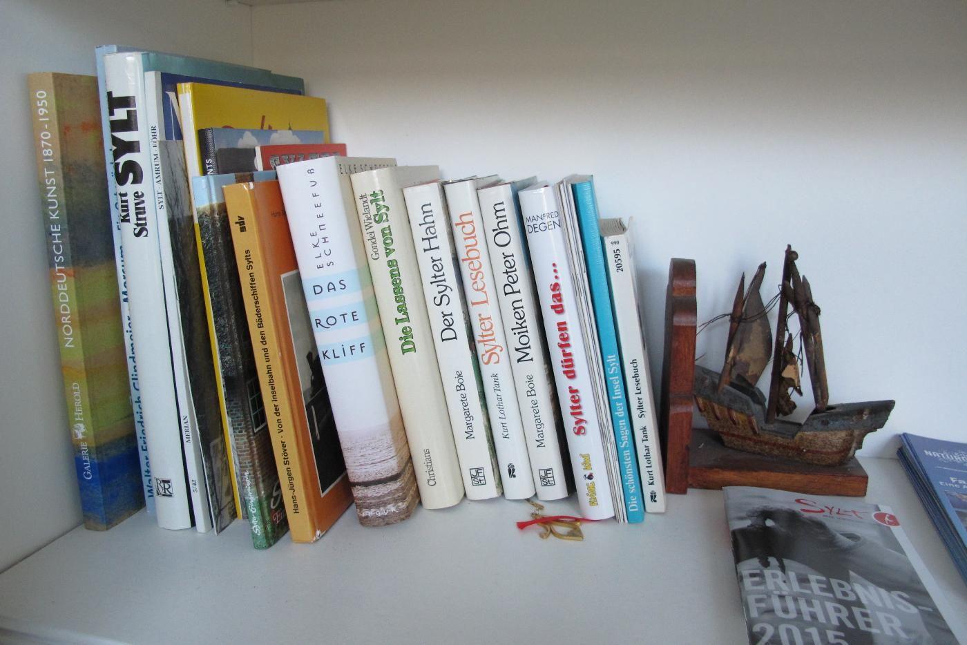 Bücherregal mit Sylter Büchern und einem hölzernen Segelschiffmodell.