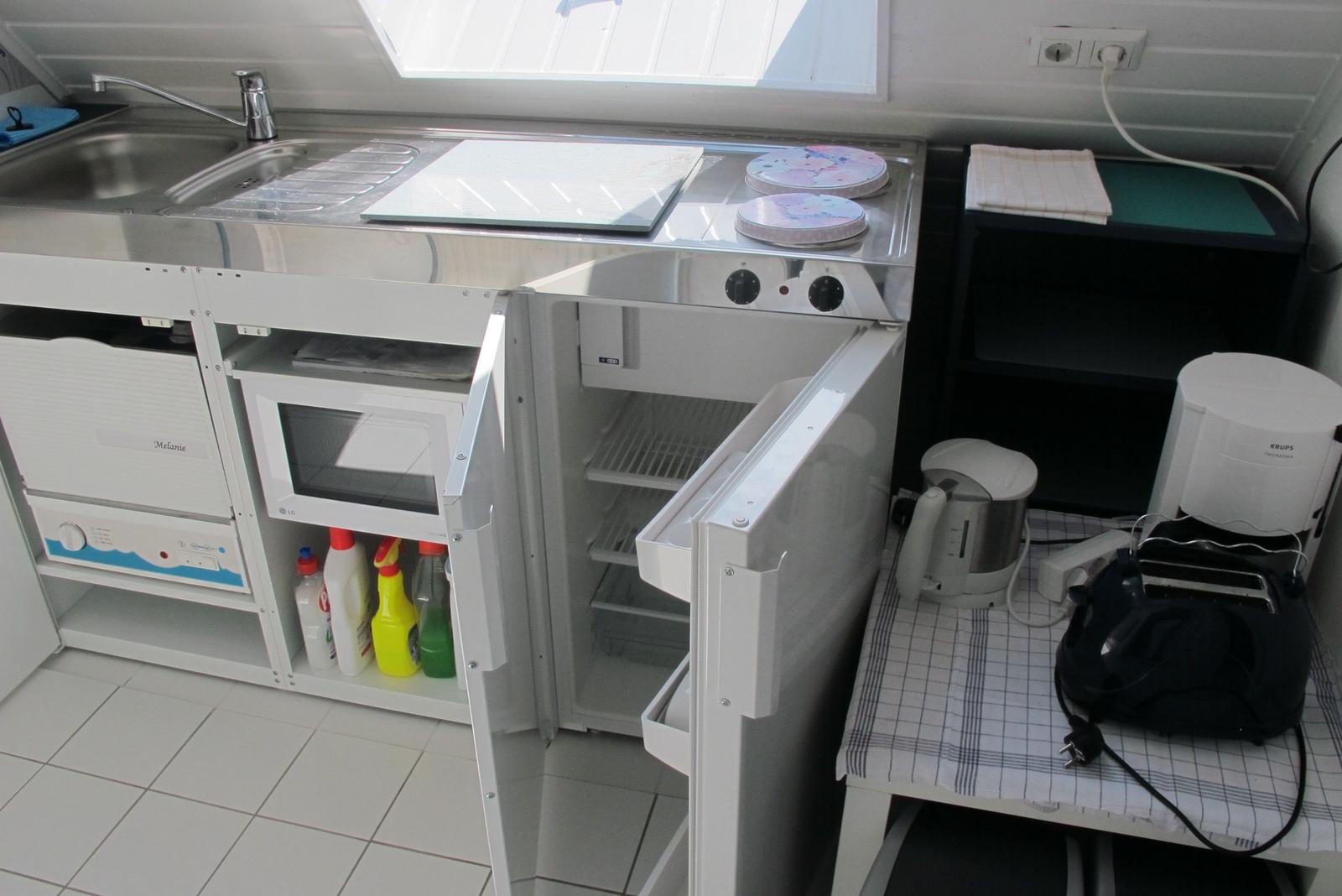 Küche mit Kühlschrank, Spüle und Kochfeld. Kühl- und Gefrierfach offen.