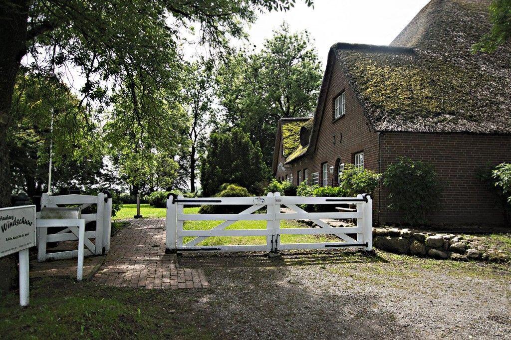 Haus mit strohgedecktem Dach, weißer Toranlage und grüner Umgebung.