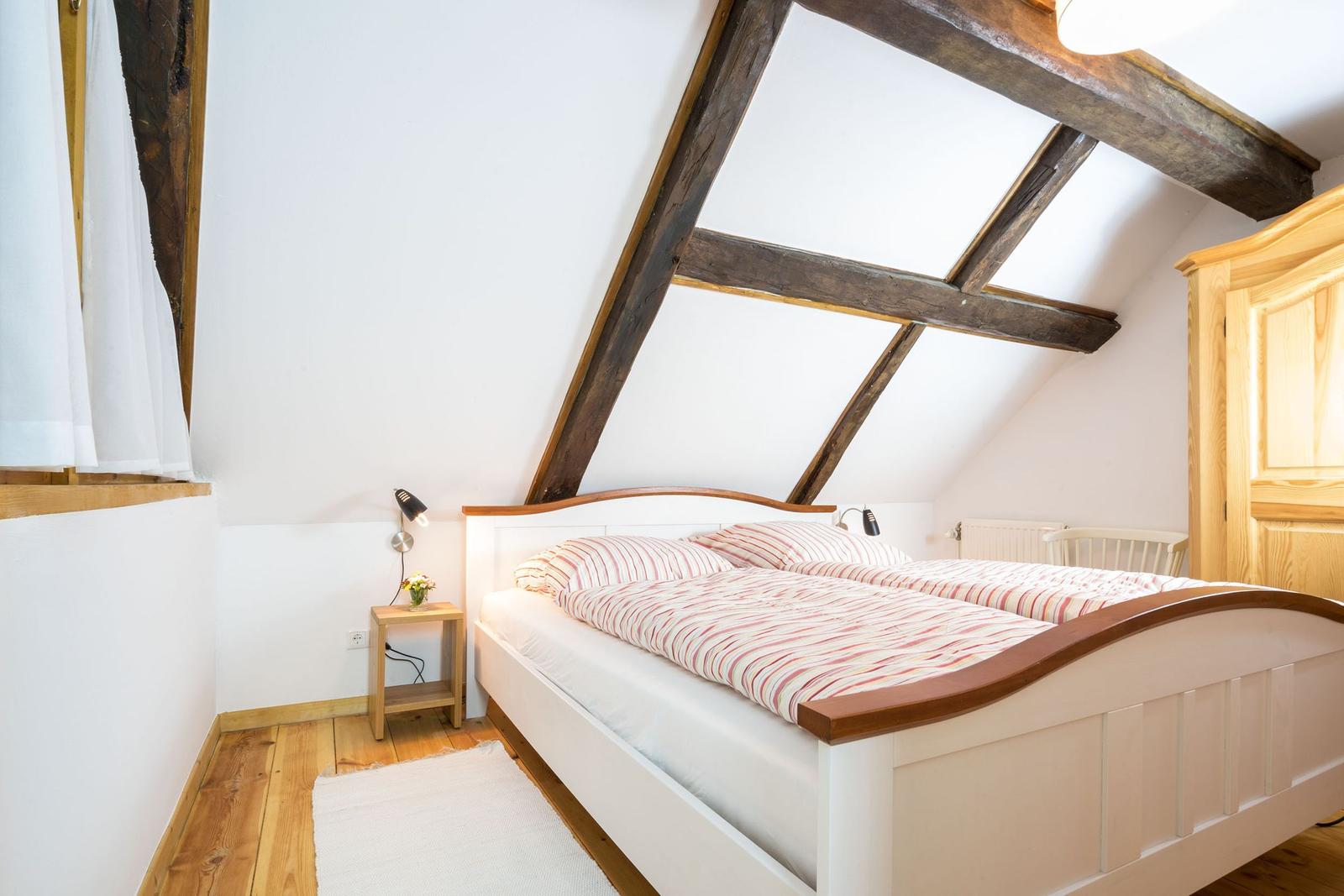 Schlafzimmer mit Dachschrägen, Holzbalken, Bett und Nachttisch.