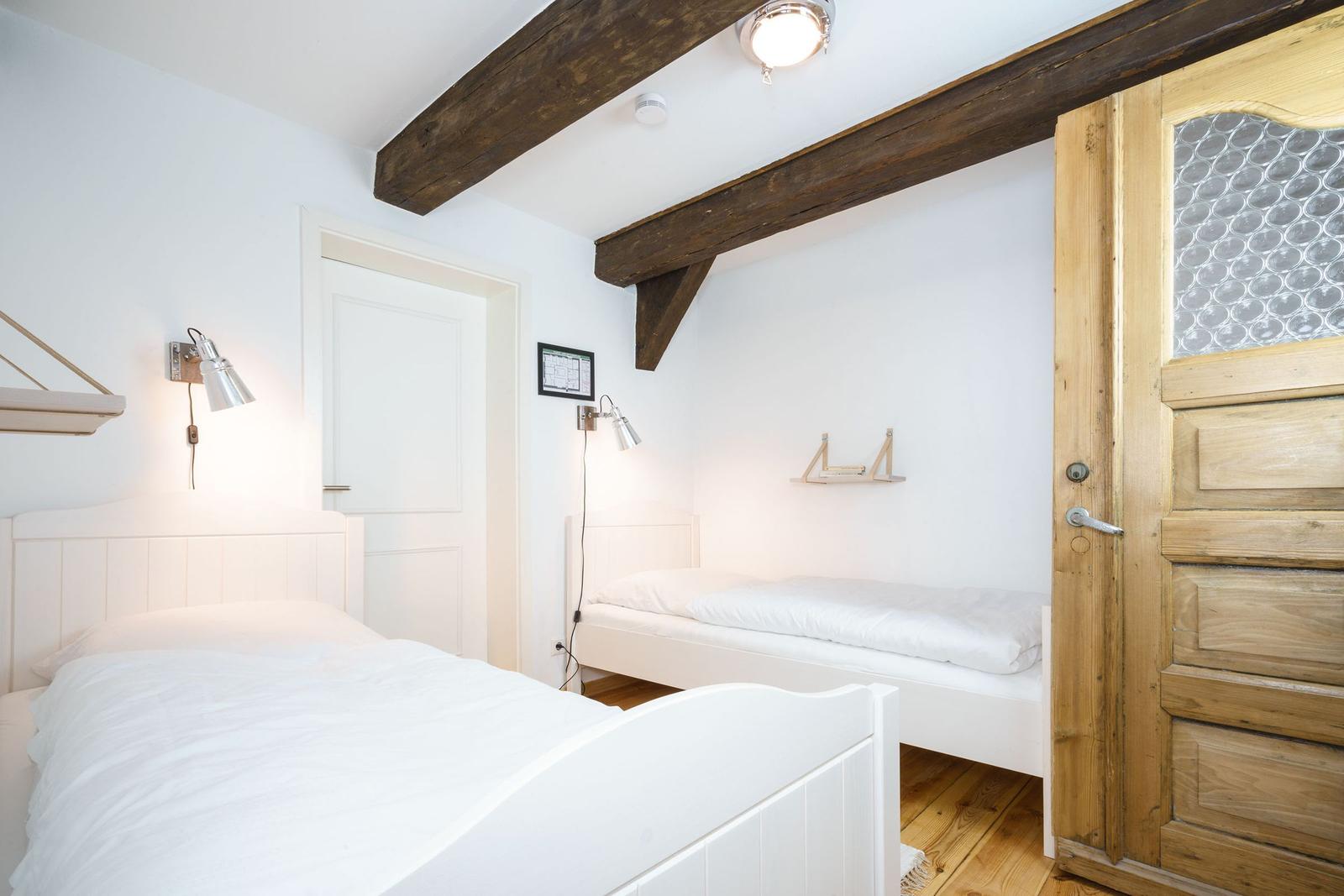 Zimmer mit zwei weißen Betten, Holzbalken an der Decke und Holztür.