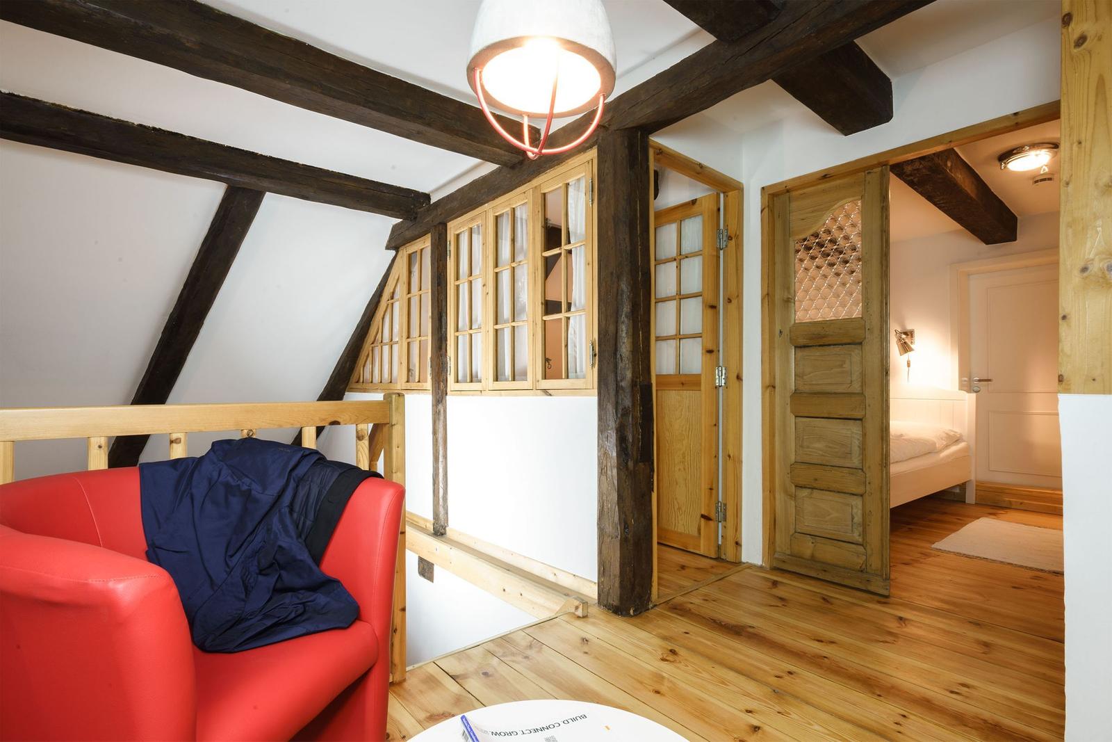 Raum mit rotem Sofa, Holzbalken und Tür zum Schlafzimmer.