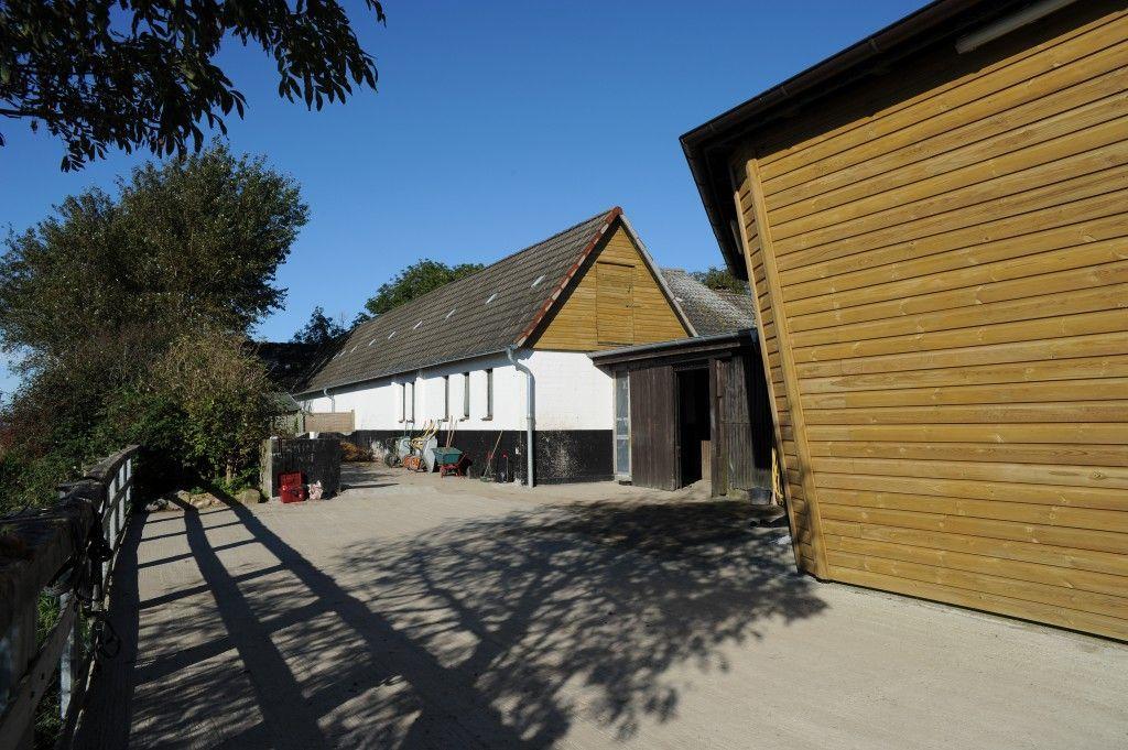 Haus mit Holzverkleidung und Dach, gepflasterter Hof, Bäume und klarer Himmel.