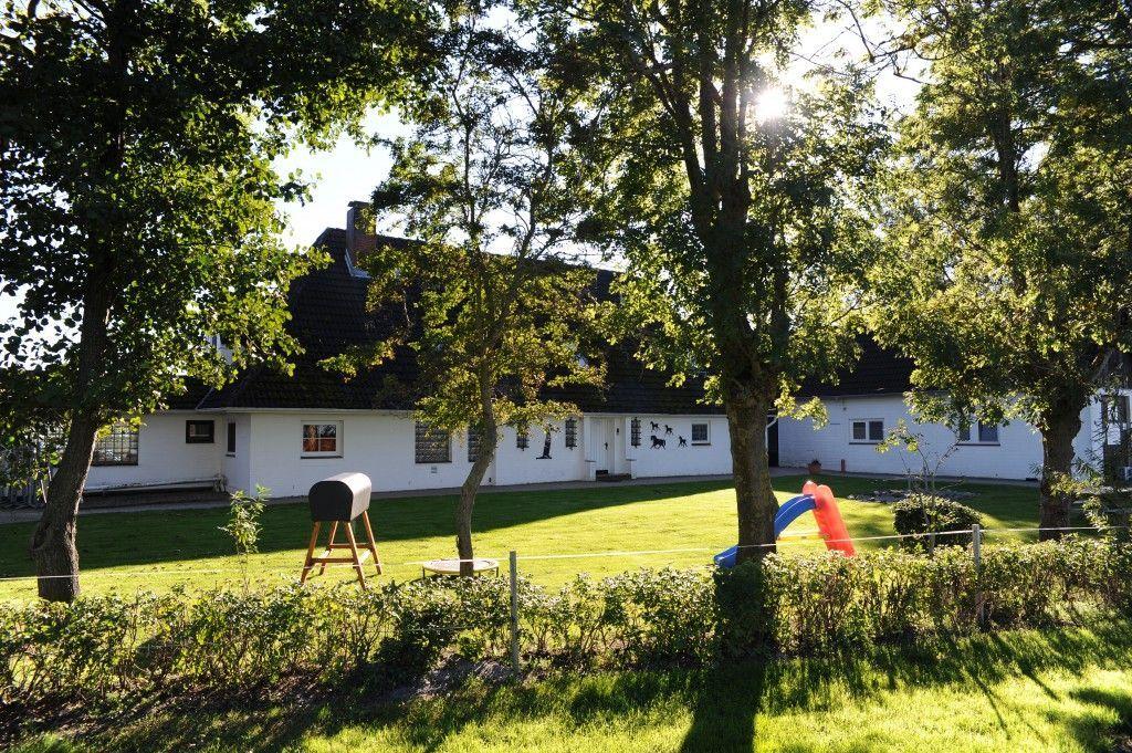 Weiße Villa mit Garten, Spielplatz und Bäumen im Hintergrund.