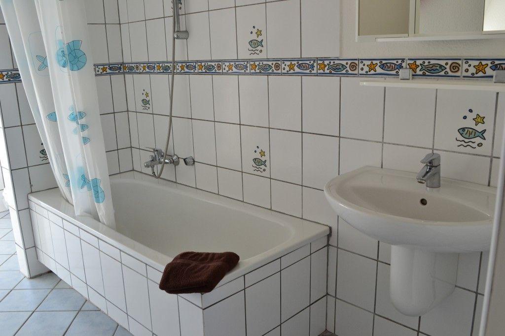 Badezimmer mit Badewanne, Waschbecken und Duschvorhang mit Fischmotiven.