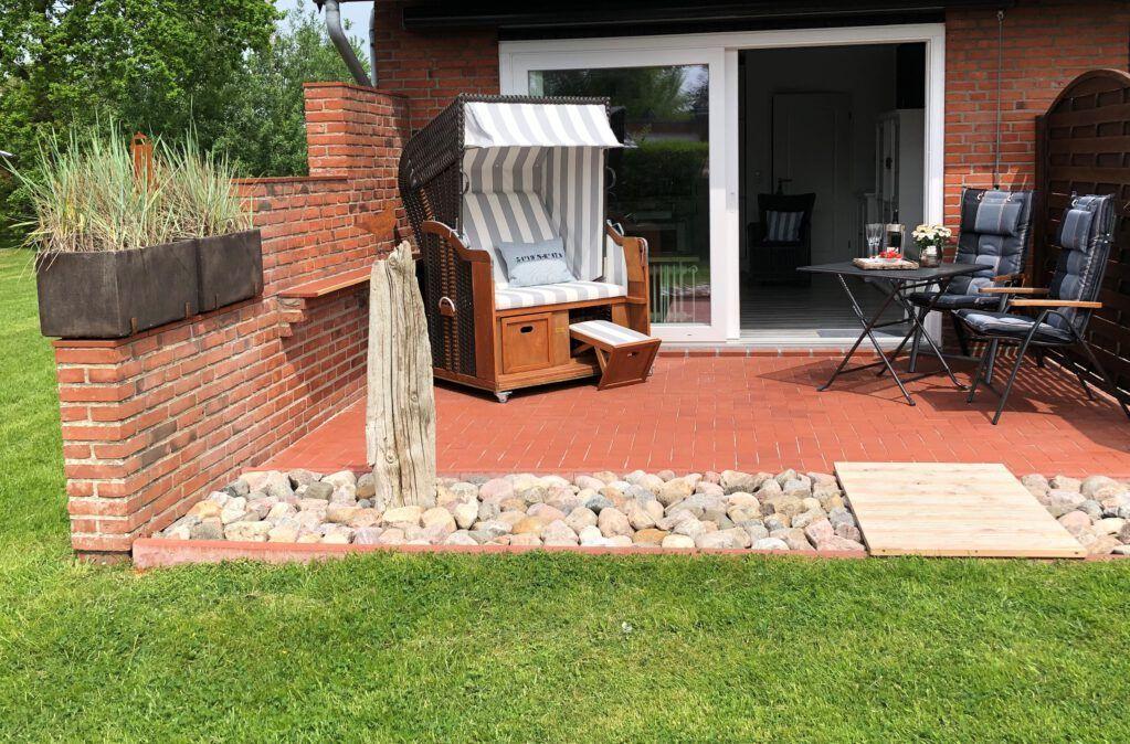 Terrasse mit Liegestuhl, Tisch und Stühlen. Hintergrund: Glasfront und Garten.