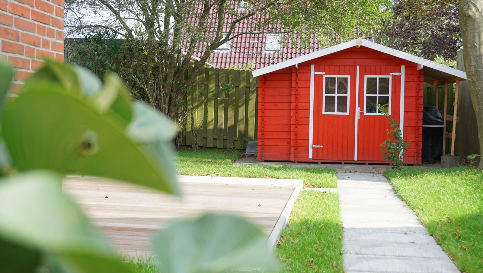Roter Holzschuppen mit weißen Fenstern und Tür im Garten.