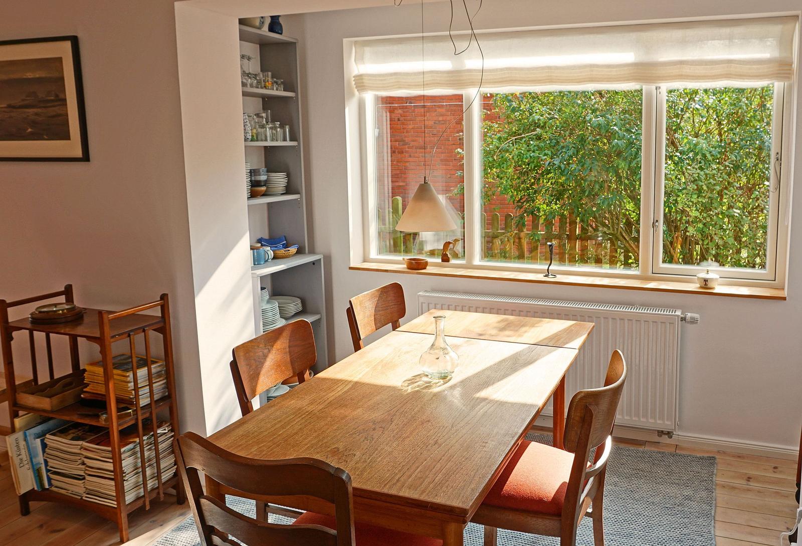 Esszimmer mit Holztisch, Stühlen und Fensterblick auf Grün.