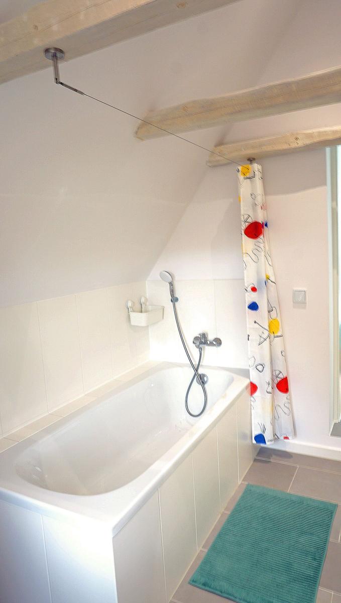 Bad mit Badewanne, Duschvorhang und Holzbalken an der Decke.