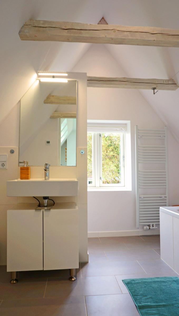 Badezimmer mit Waschbecken, Spiegel und Fenster. Holzbalken an der Decke.
