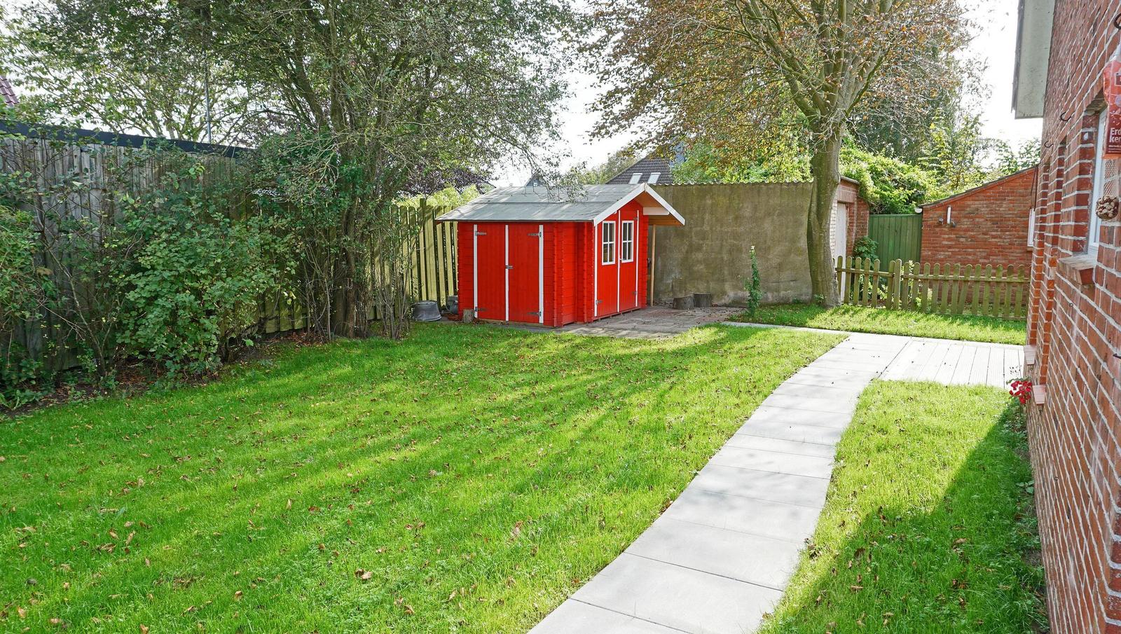 Roter Holzschuppen im Garten mit Weg und Grasflächen.