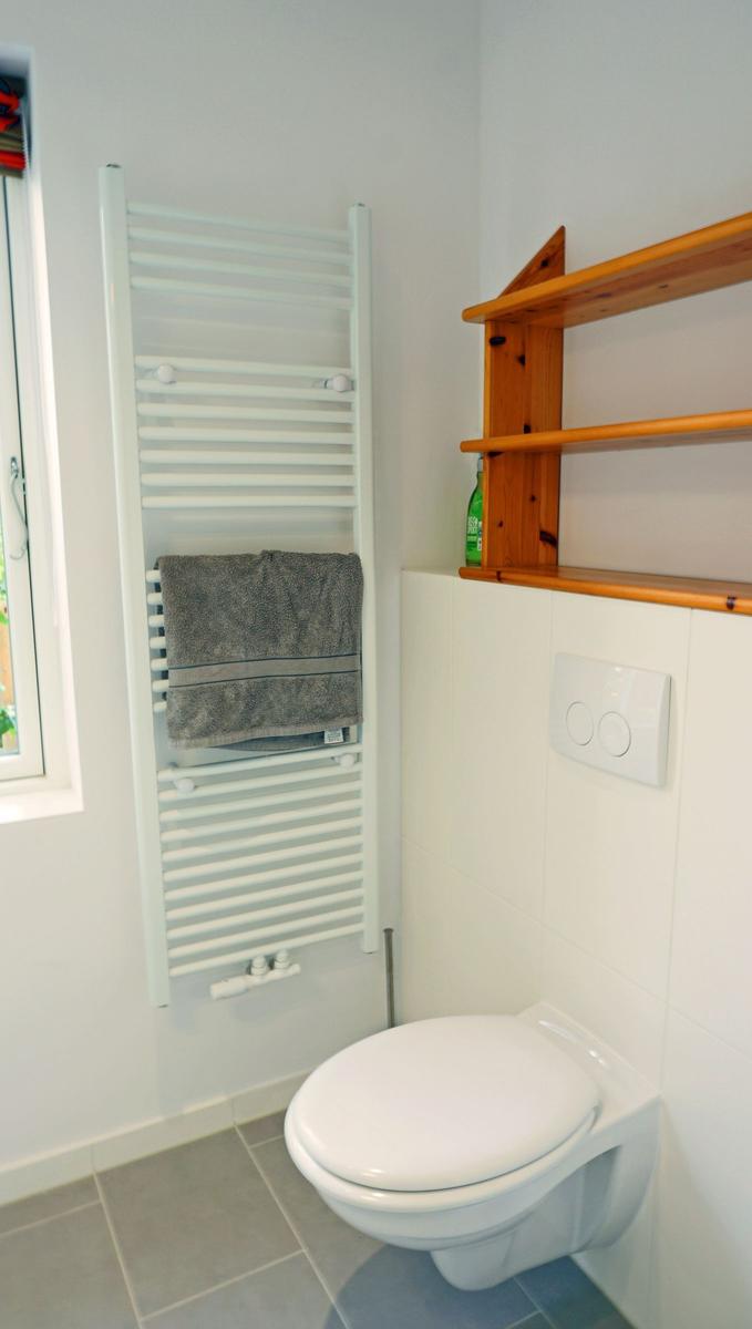 Badezimmer mit Toilette, Heizkörper und Holzregal an der Wand.