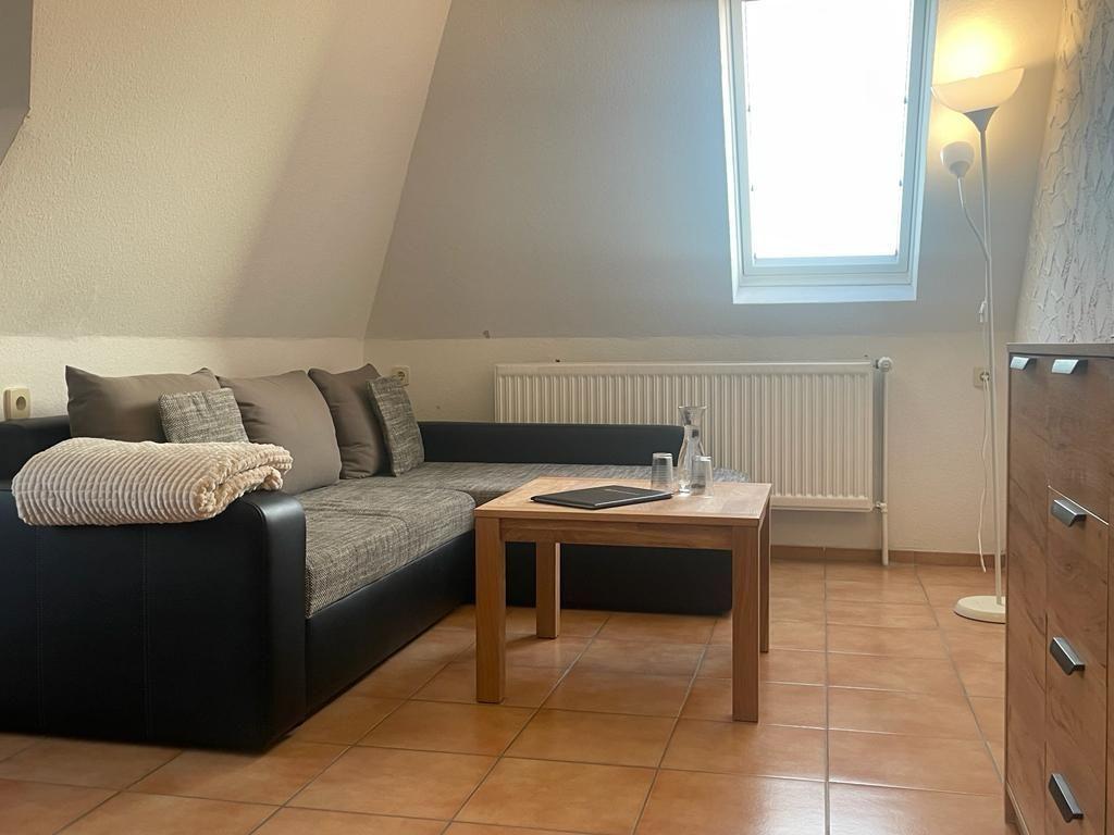 Wohnzimmer mit Sofa, Tisch und Fenster unter schrägen Dachdecken.