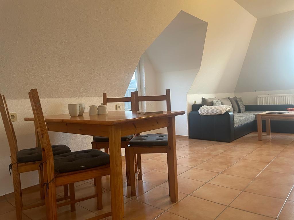 Essbereich mit Holztisch und Stühlen. Im Hintergrund befindet sich ein Sofa.