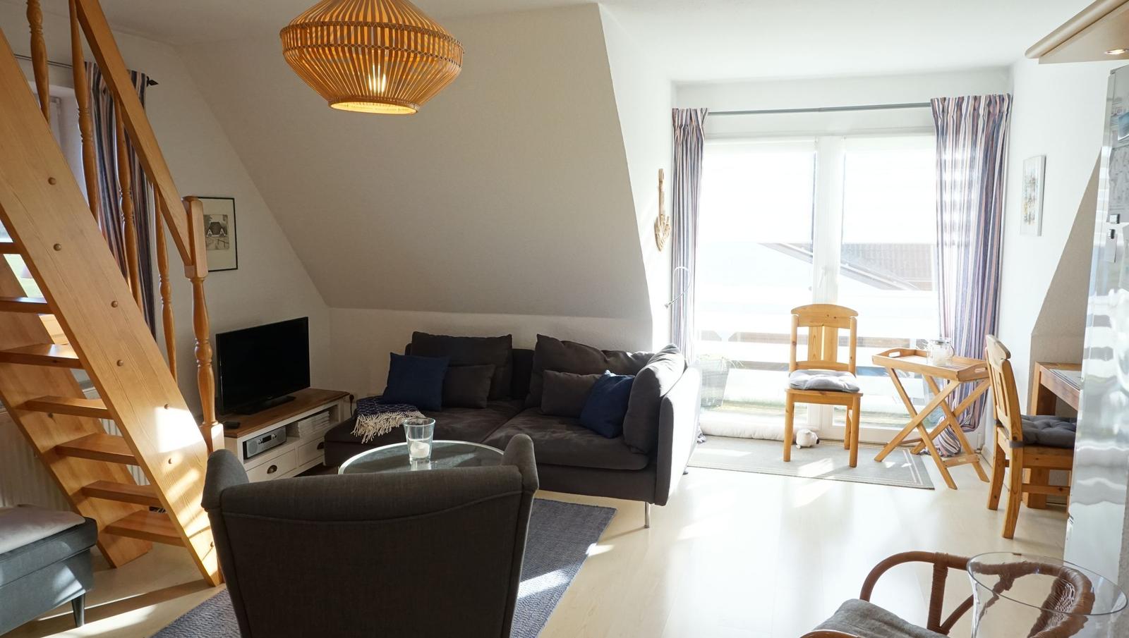 Wohnzimmer mit Sofa, Fernseher und Holztreppe zur oberen Etage.