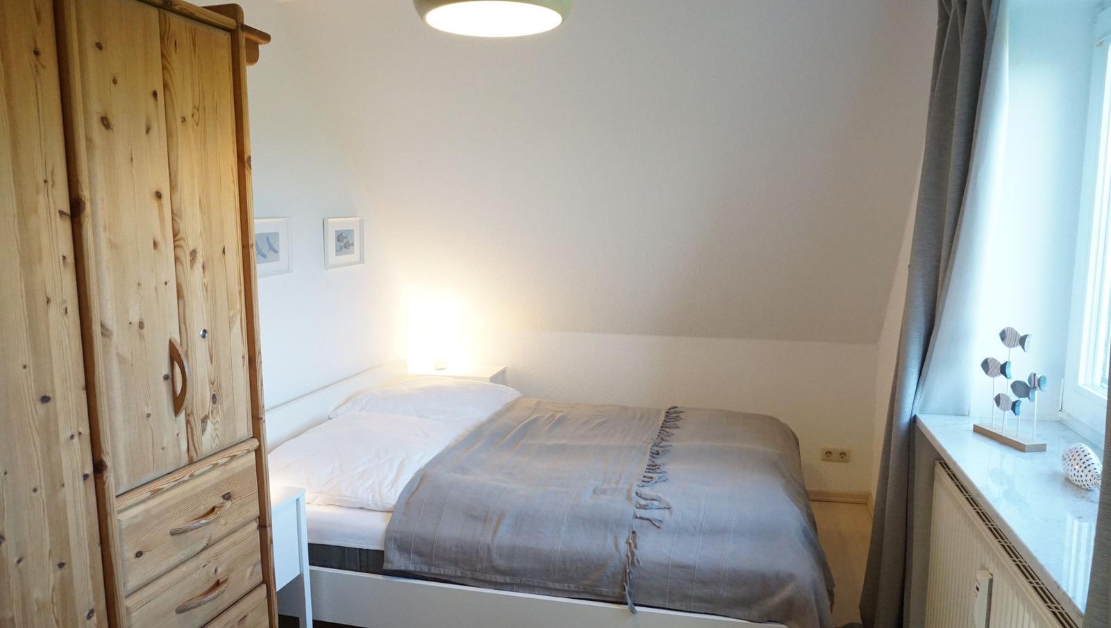 Schlafzimmer mit Bett, Holzschrank und Fenster mit Vorhängen.