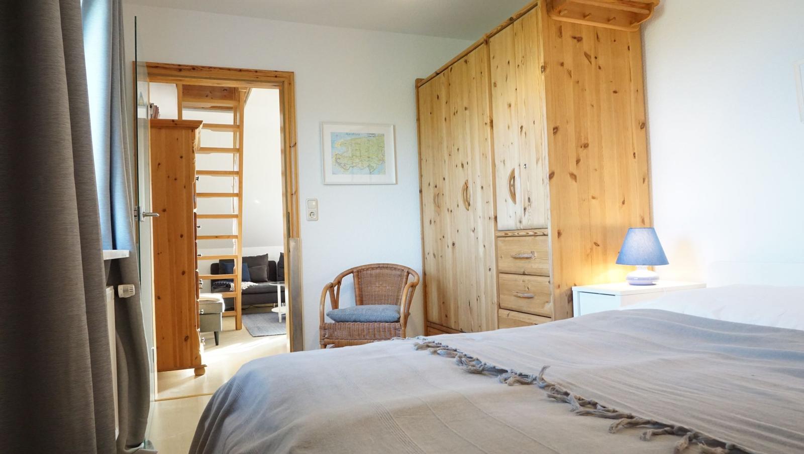 Schlafzimmer mit Bett, Holzschrank und Blick in Wohnbereich mit Sofa.
