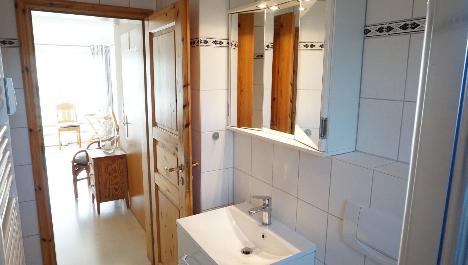 Badezimmer mit Waschbecken, Spiegel und Tür zum angrenzenden Raum.