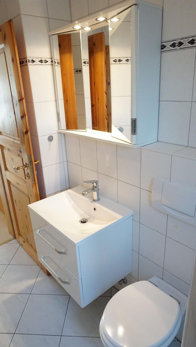 Badezimmer mit Waschbecken, Spiegelschrank und Toilette. Fliesenwand und Holztür.