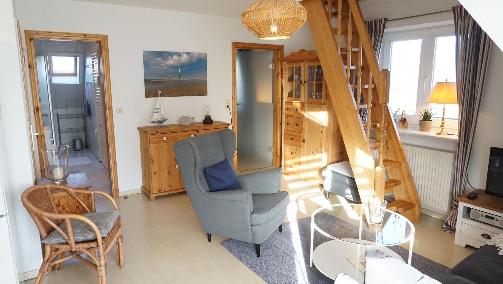 Wohnzimmer mit Holztreppe, Sessel und Glas-Tisch. Blick in Bad und Schlafzimmer.