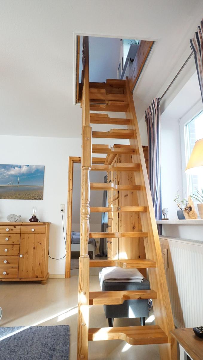 Holztreppe führt zu einer oberen Etage. Im Hintergrund sind Möbel und ein Fenster sichtbar.