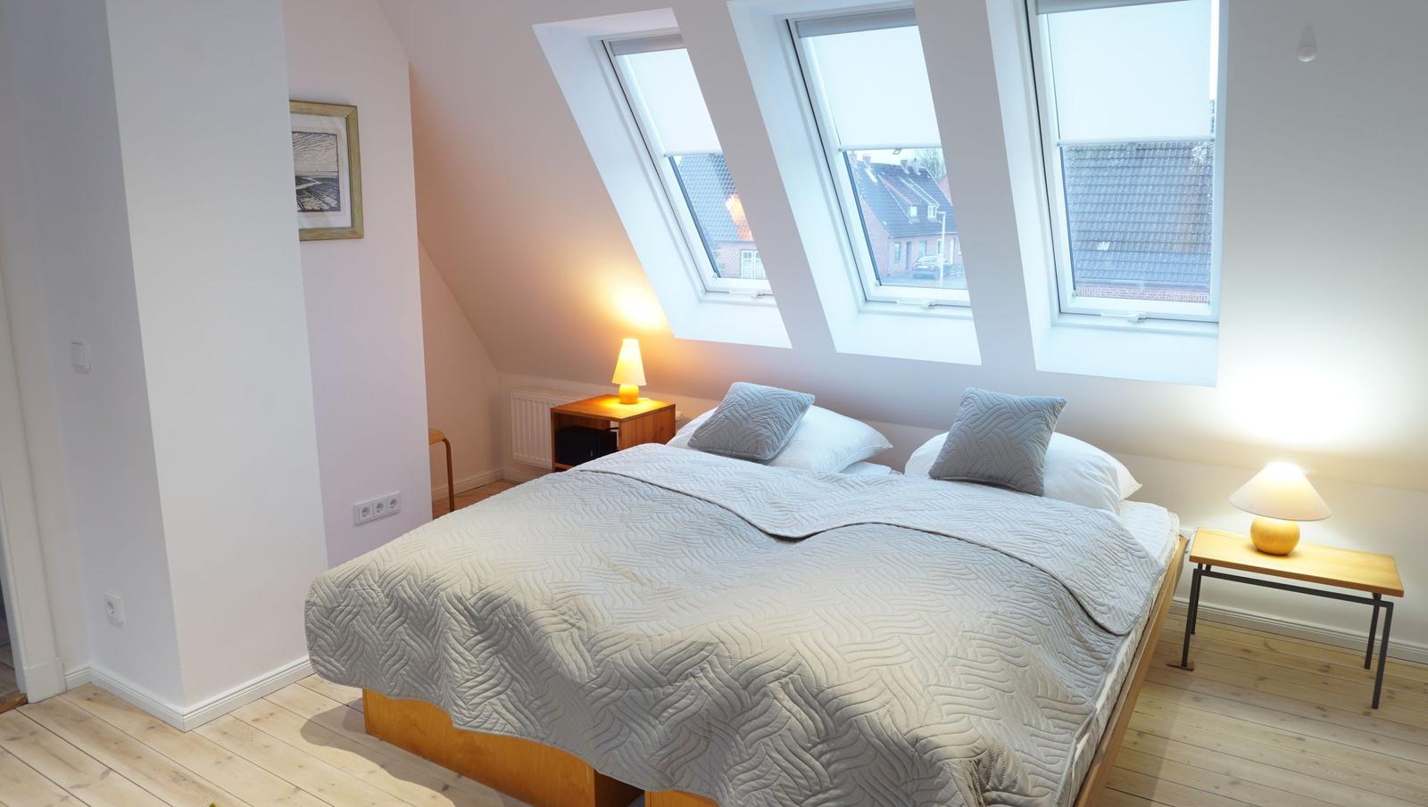 Schlafzimmer mit Dachschrägen, drei Dachfenstern und Holzboden.