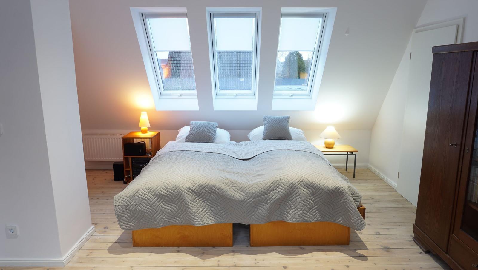 Schlafzimmer mit Dachfenstern, Bett, Nachttischen und Schrank.