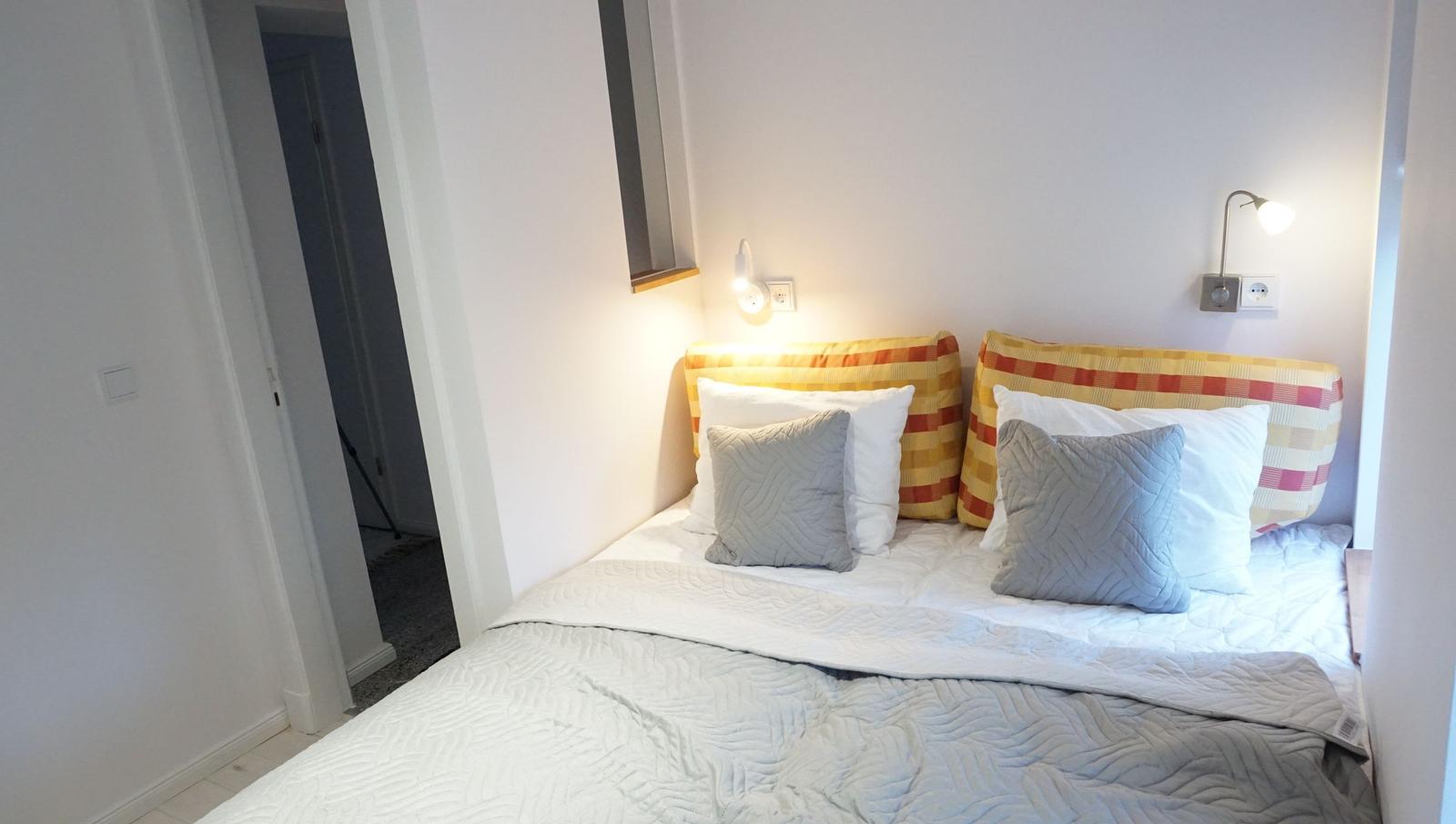 Schlafzimmer mit Bett, Kissen und Wandlampen.