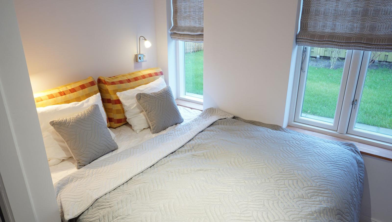 Schlafzimmer mit Bett, Kissen und Fensterblick auf einen Garten.