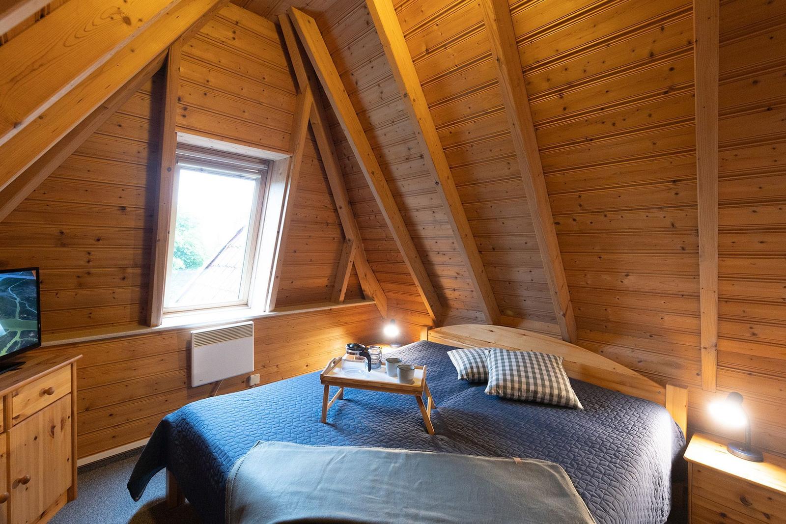 Bedroom with wooden walls, sloped ceiling, bed, and window