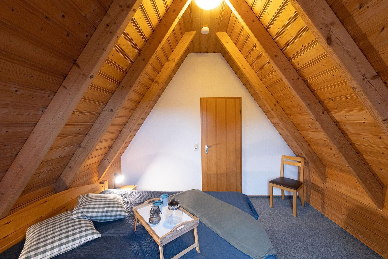 Attic room with wooden ceiling, bed, chair, and table.
