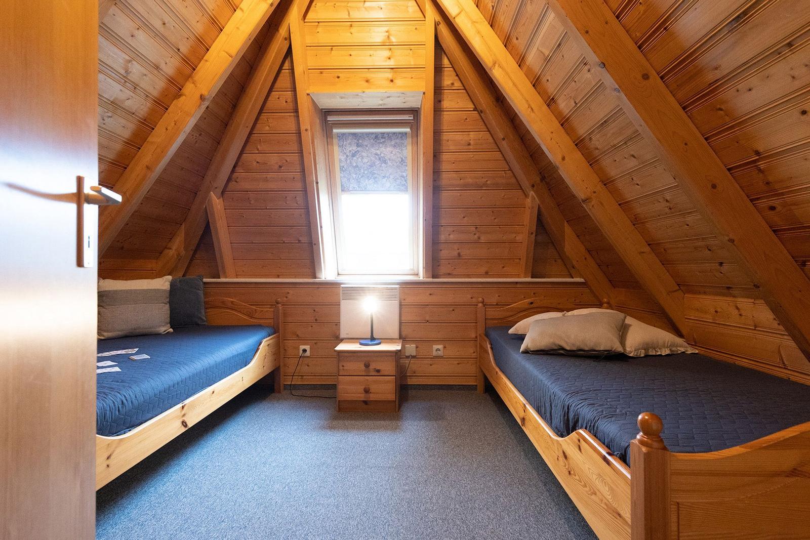 Two single beds under wooden ceiling with window and nightstand.