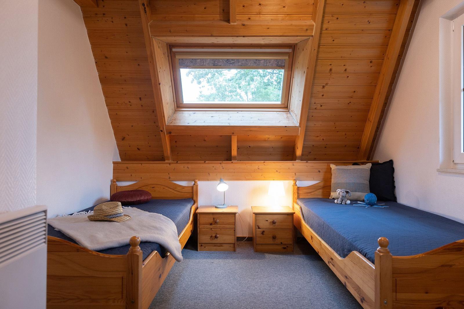 Two single beds with nightstands under a skylight in a wooden room.