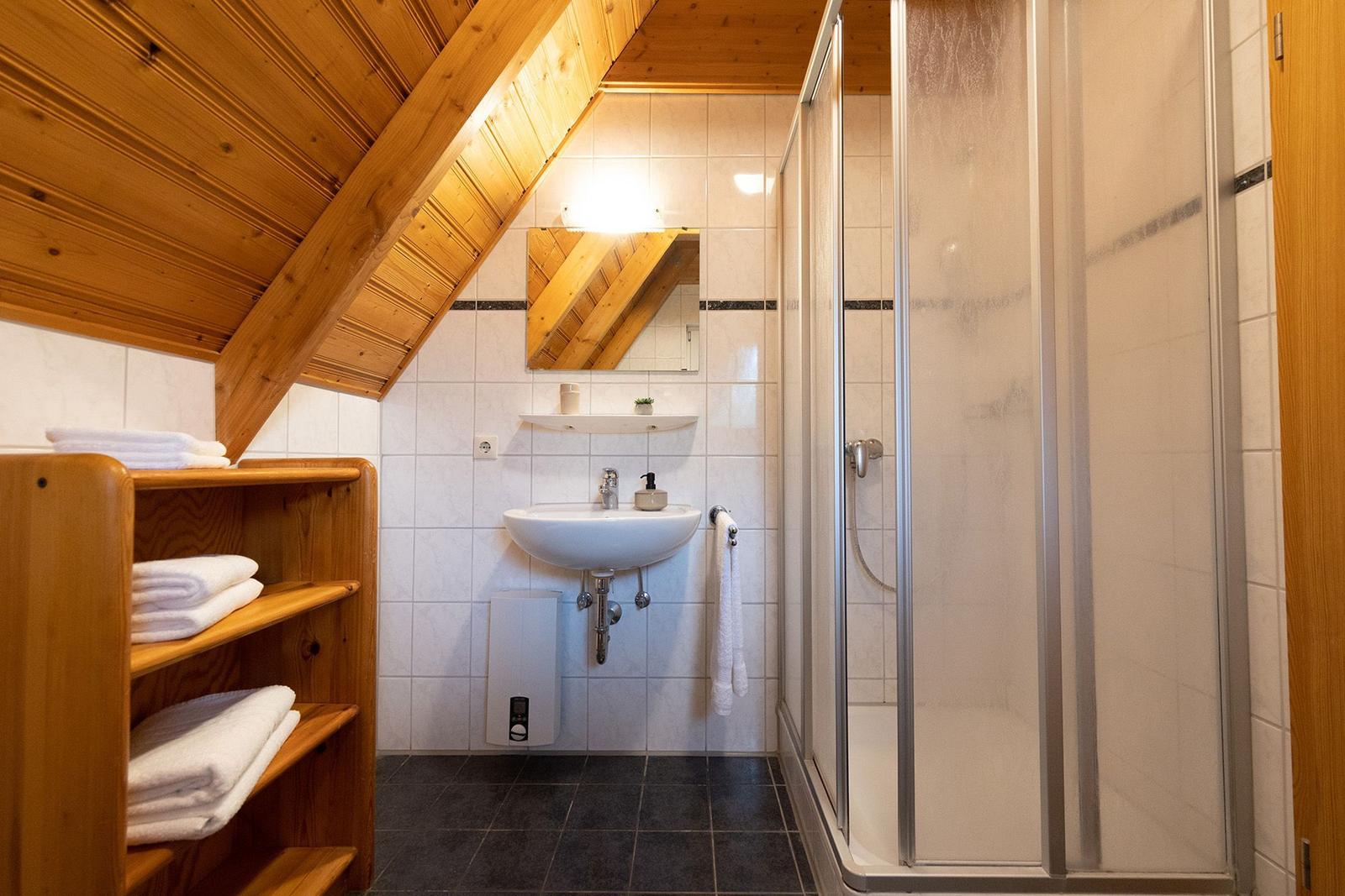 Bathroom with shower, sink, and wooden shelf with towels.
