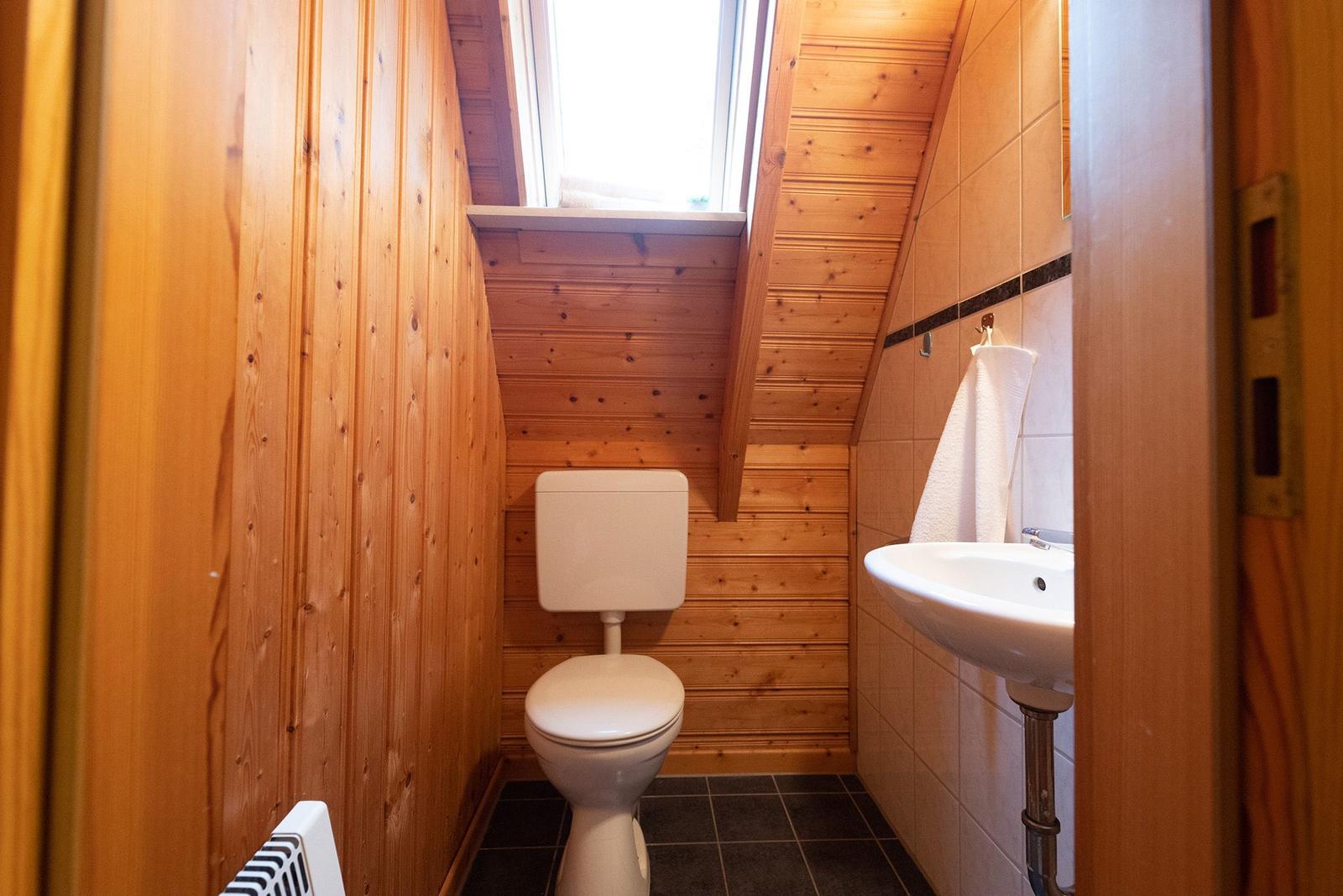 Bathroom with toilet, sink, and sloped ceiling. Wooden walls and window.