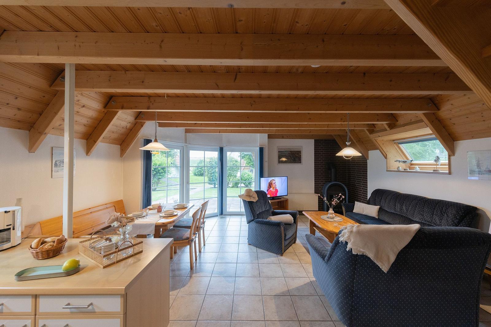 Living and dining area with wooden ceiling, sofa, TV, and terrace door.
