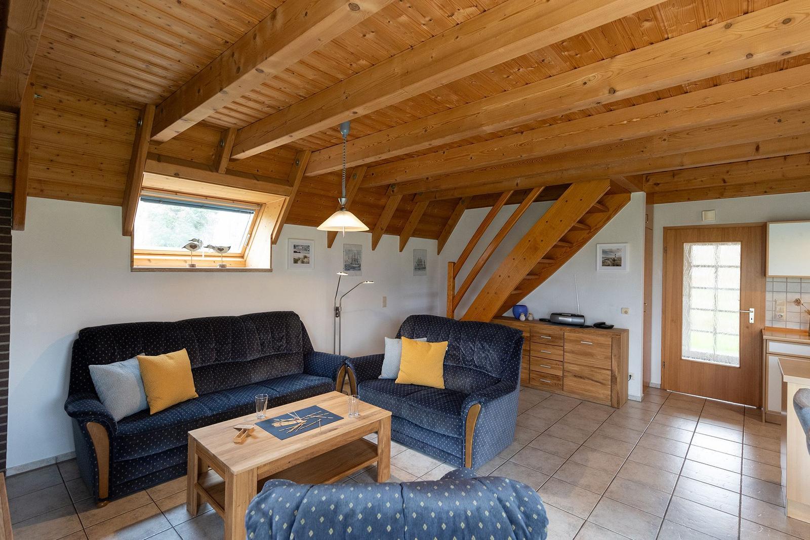 Living room with wooden ceiling, sofa, coffee table, and staircase.