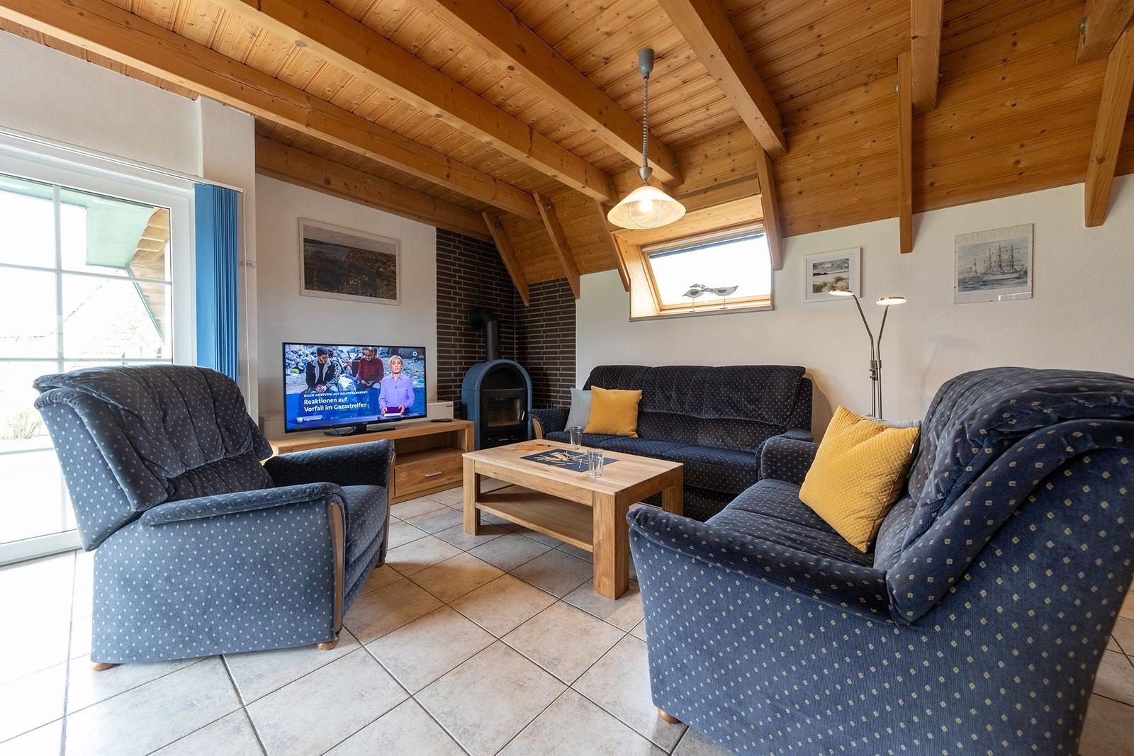 Living room with sofa, two armchairs, wooden table, and fireplace under wooden beam ceiling.