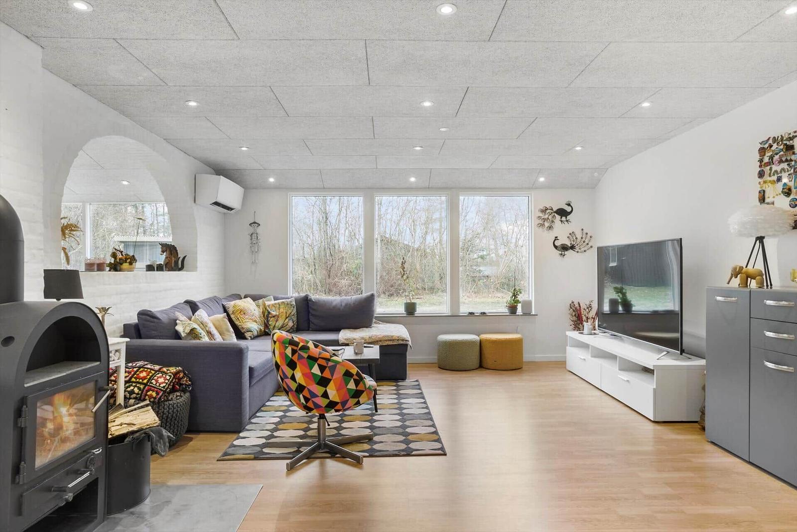 Wohnzimmer mit Sofa, Kamin, TV und großen Fenstern.