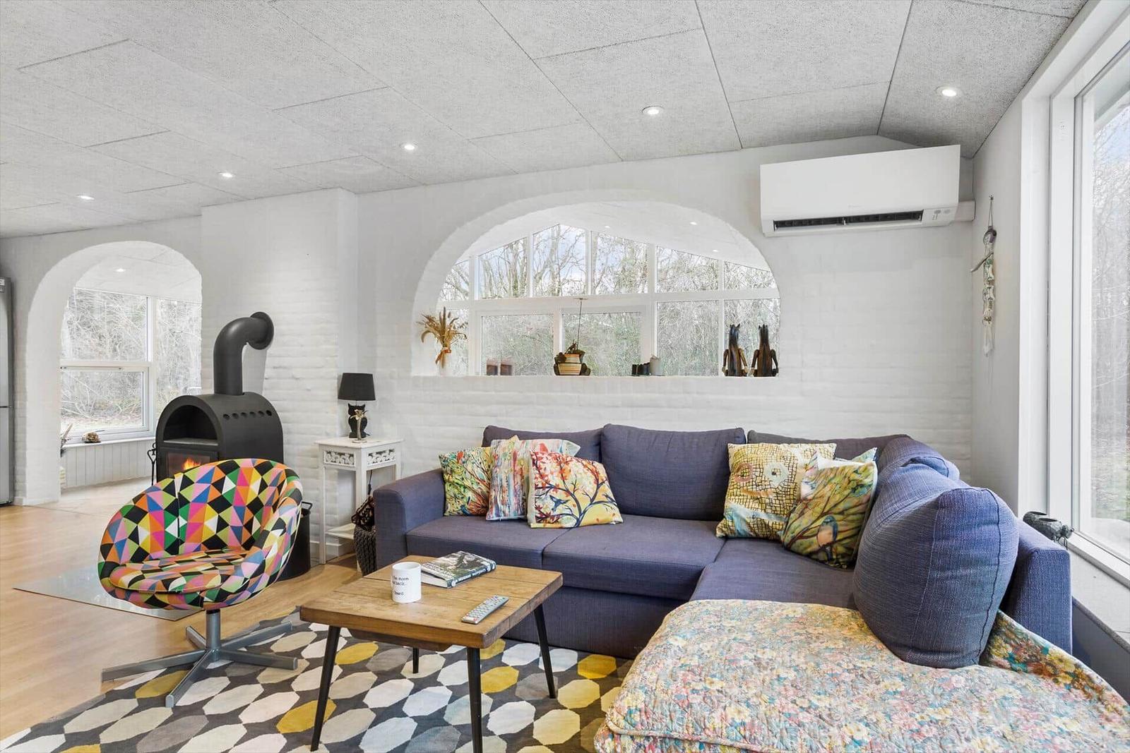 Wohnzimmer mit Sofa, Kamin und Bogenfenster. Bunt gemusterte Sitzgelegenheiten.