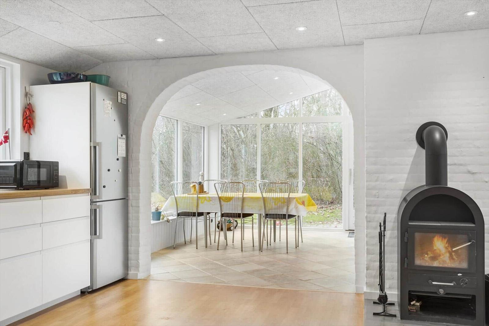 Küche mit Kühlschrank und Mikrowelle. Durch Bogen führt zur Essnische mit Tisch und Stühlen.