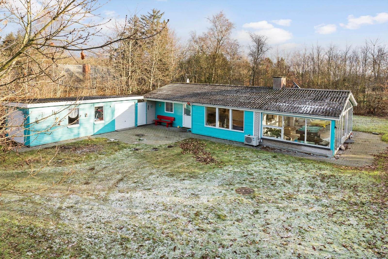 Ein türkisfarbenes Haus mit großem Wintergarten und roter Bank im Garten.