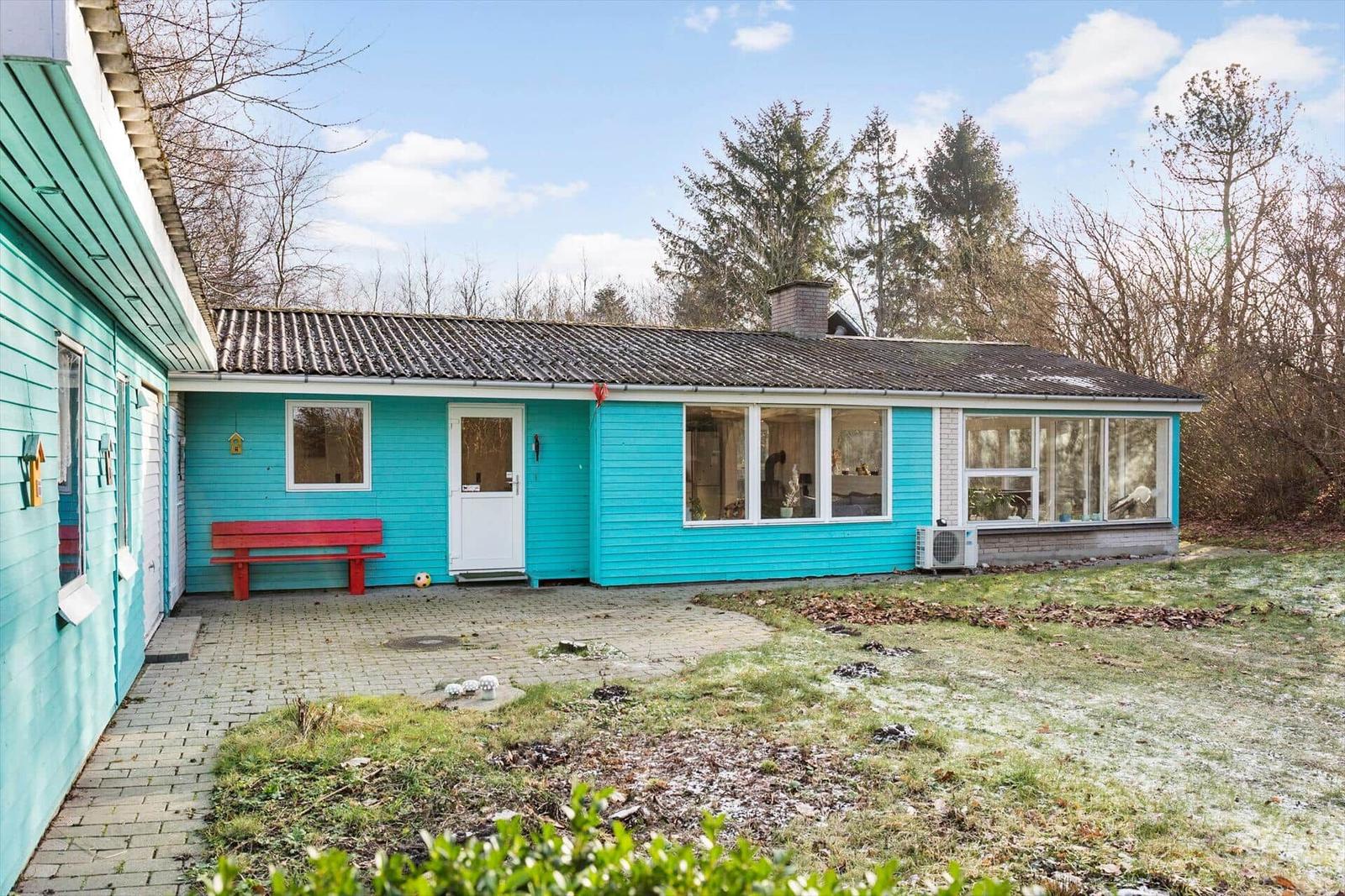 Ein türkisfarbenes Haus mit roter Bank vorne und großen Fenstern.