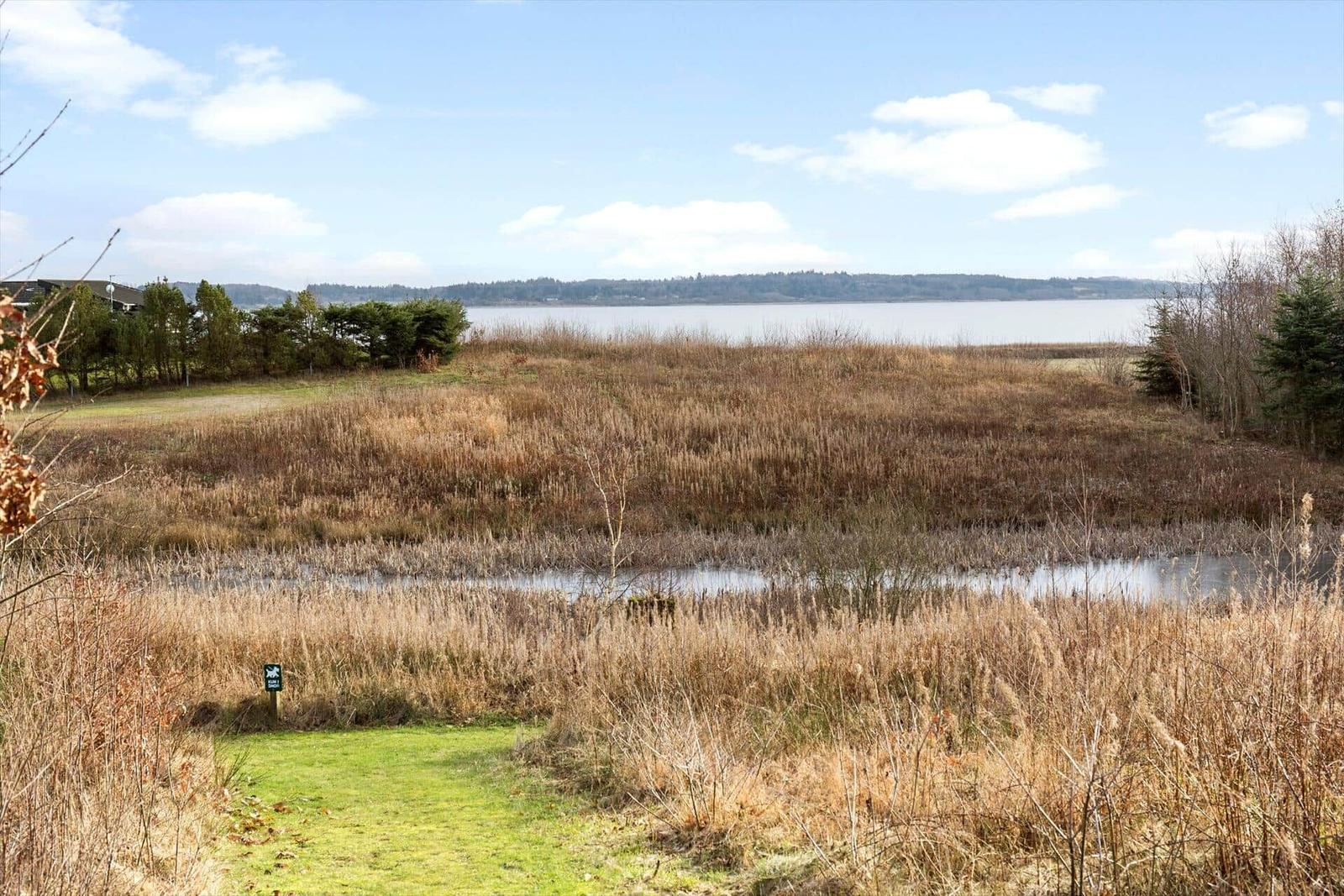 Wiesenlandschaft mit Fluss und Blick auf einen See unter blauem Himmel.