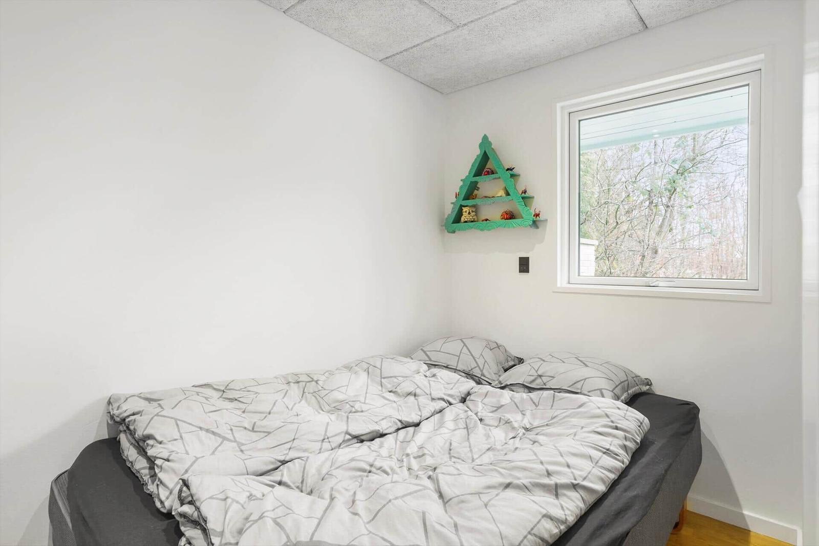 Schlafzimmer mit Bett, Fenster und grünem Wandregal.