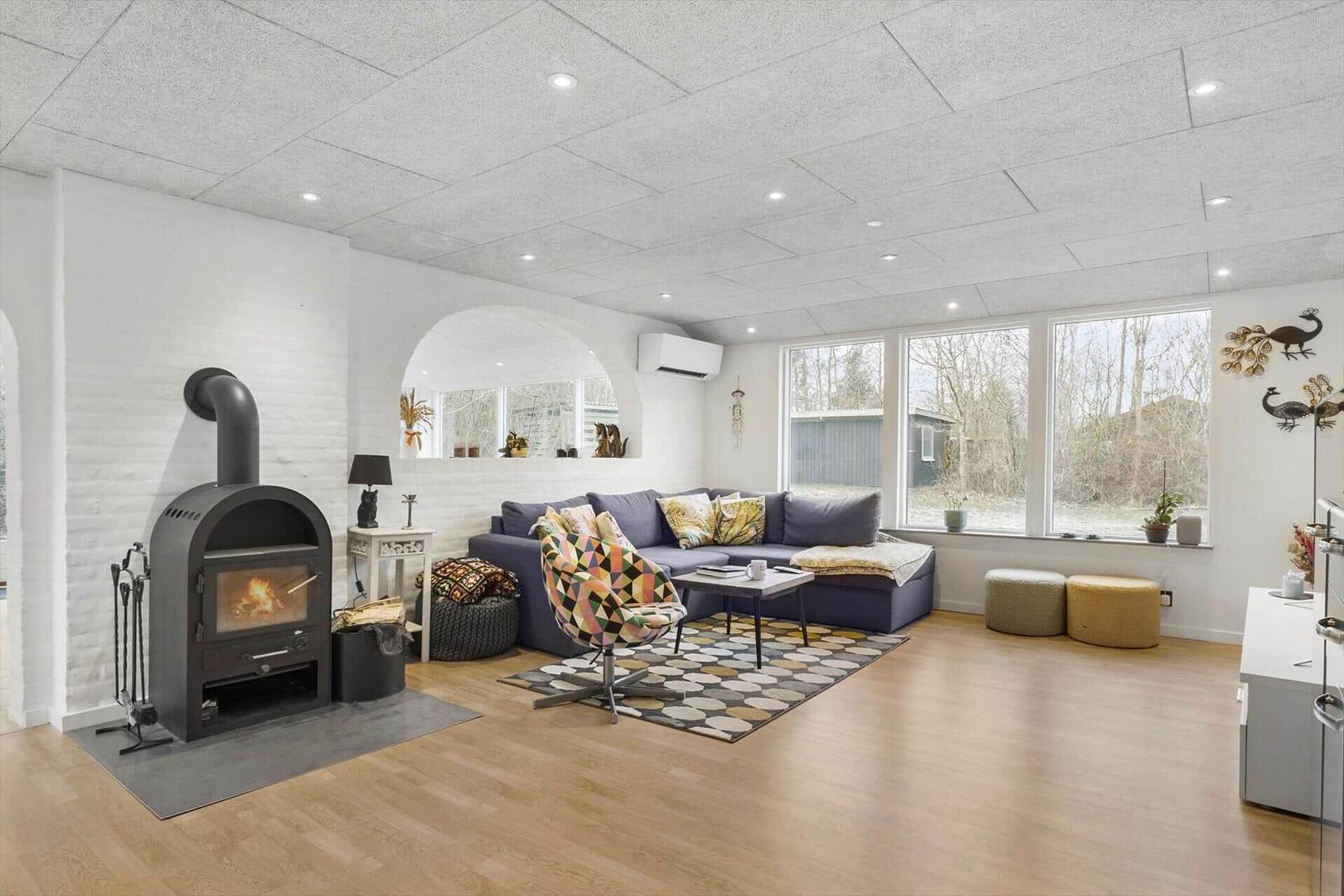Wohnzimmer mit Kamin, Sofa und Fenstern. Holzboden und weißer Putz.