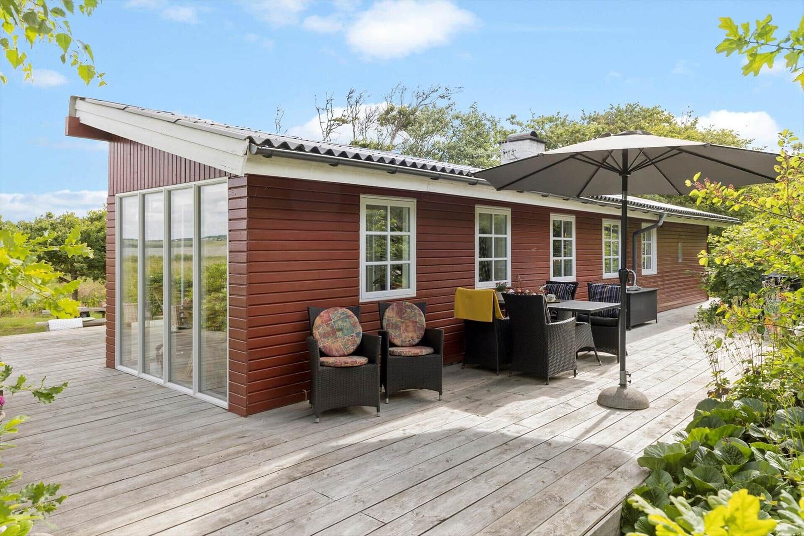 Rotes Holzhaus mit Terrasse, Sitzgruppe und Sonnenschutz. Grün umgeben.
