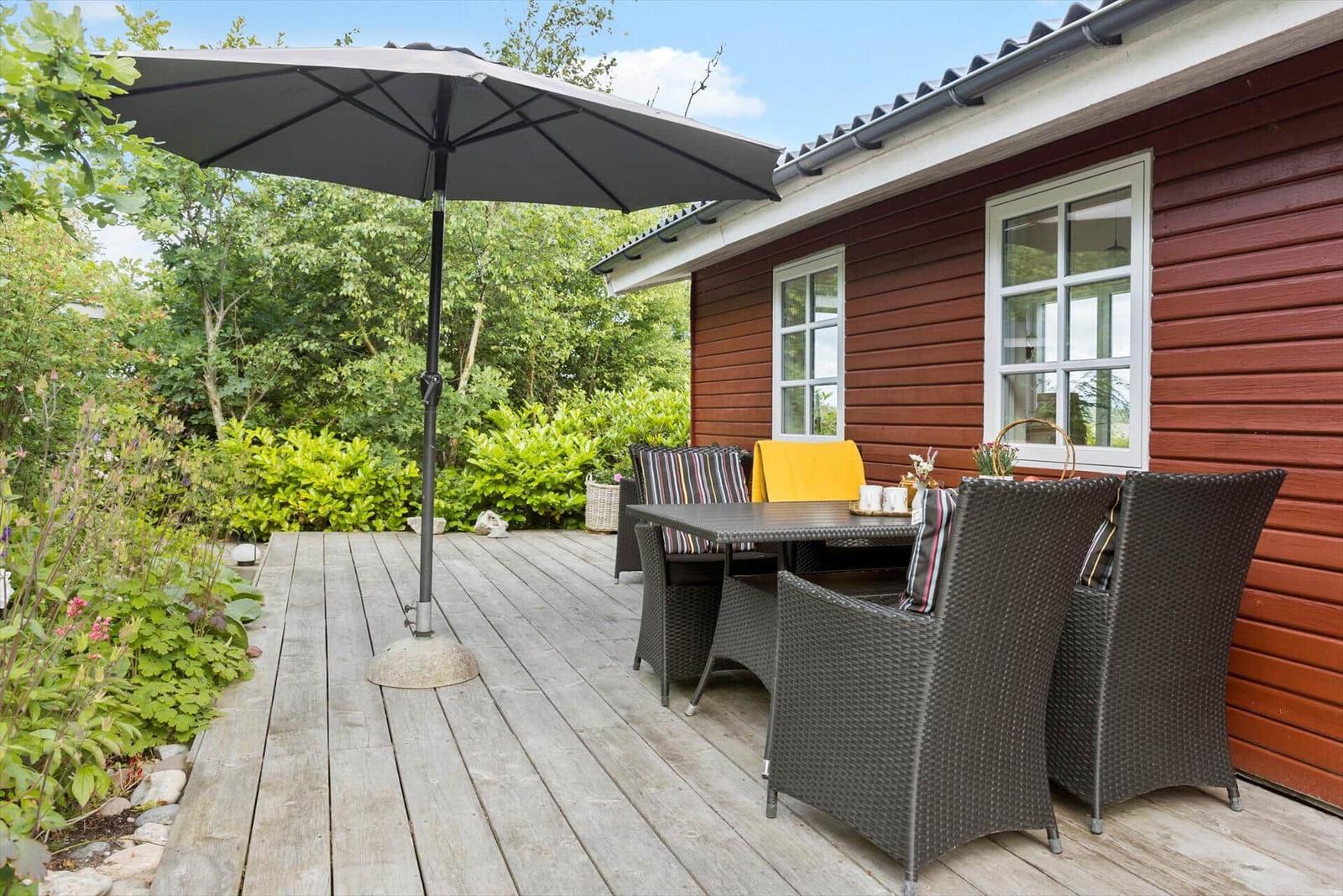Terrasse mit Tisch, Stühlen und Sonnenschirm neben rotem Holzhaus.