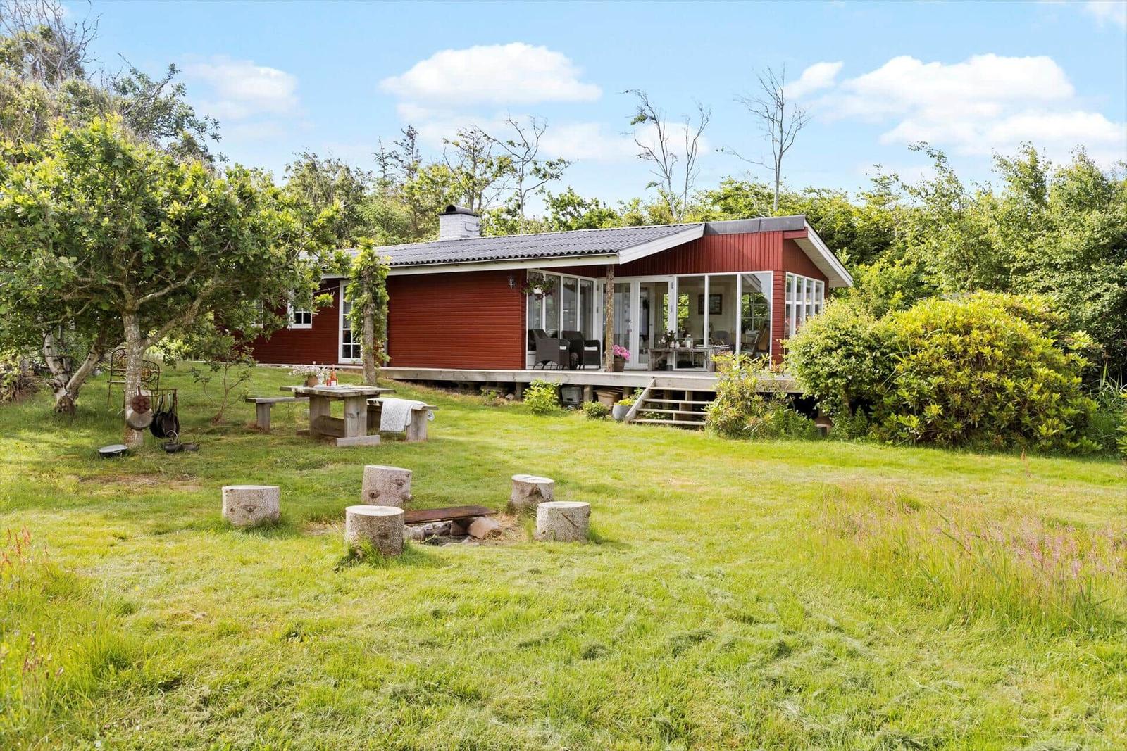 Rotes Haus mit Terrasse, Grillplatz und Garten. Umgeben von Bäumen und Gras.