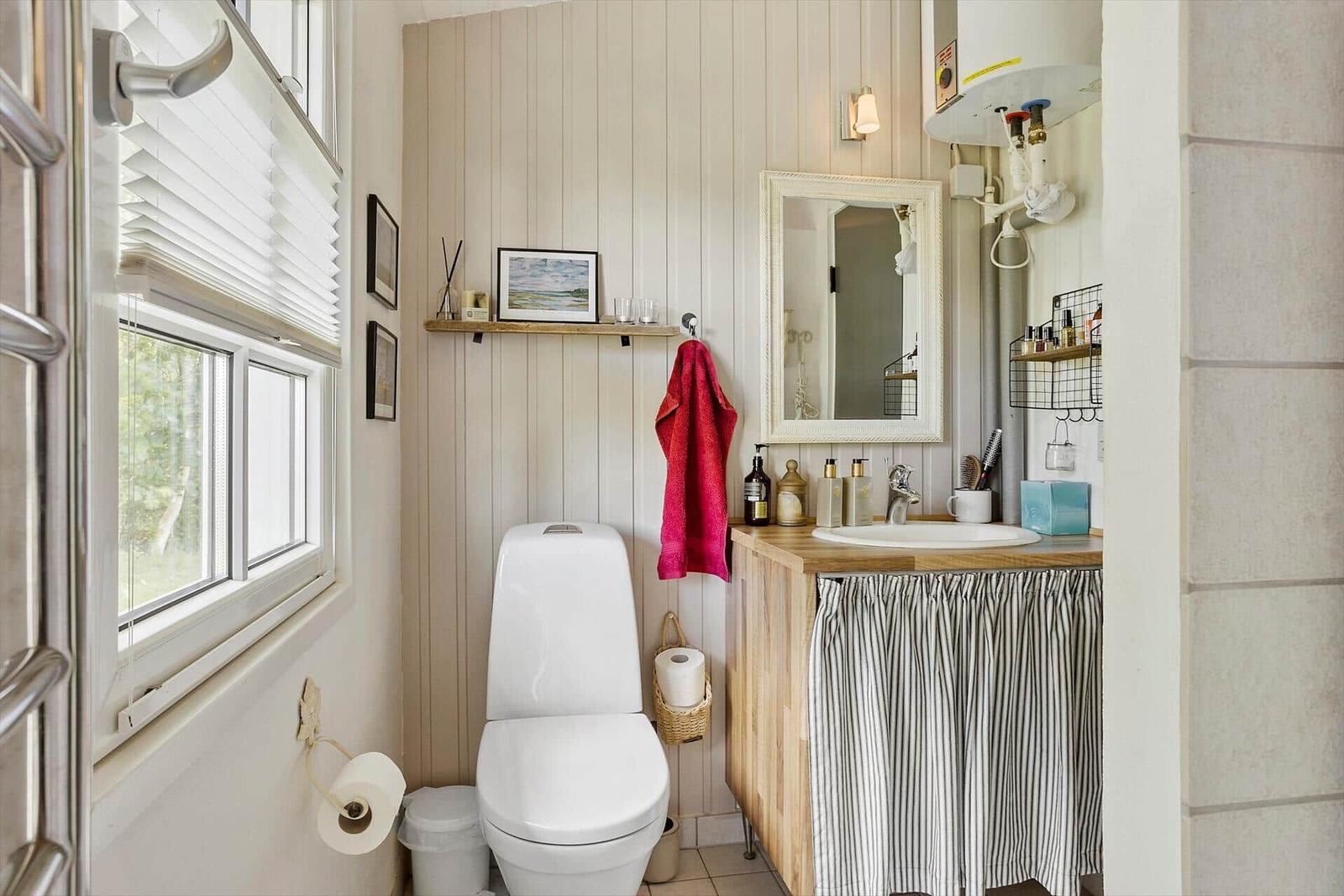 Badezimmer mit Toilette, Waschbecken und Fenster. Wandverkleidung und Holzoberfläche.